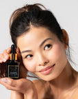 Woman holding A black bottle with a dropper of Cocomero Watermelon Glow Serum with Hyaluronic Acid, labeled with the brand Bella Vida Santa Barbara luxury skincare, and an award badge for 'Beauty Shortlist Editor's Choice 2024'. The product is described as helping to achieve a glow and radiance for the skin.